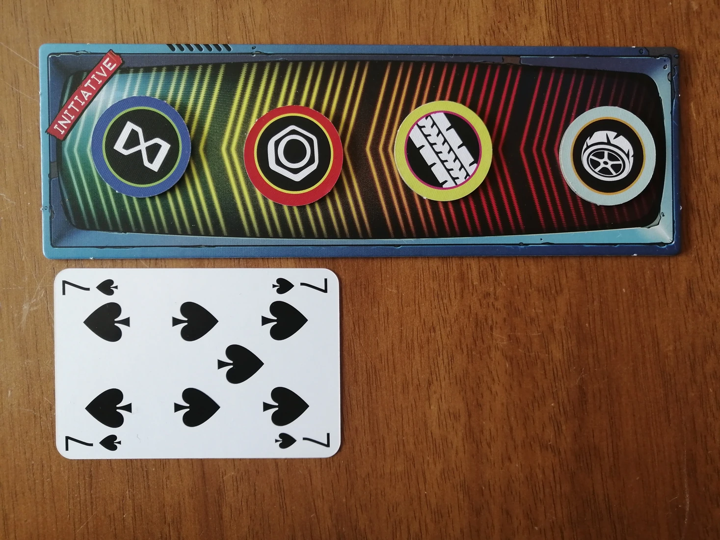 The initiative track, and initiative tokens next to a standard playing card. The track is approximately twice the height of the card and the same width as the card. The tokens are circular and under half the width of the card