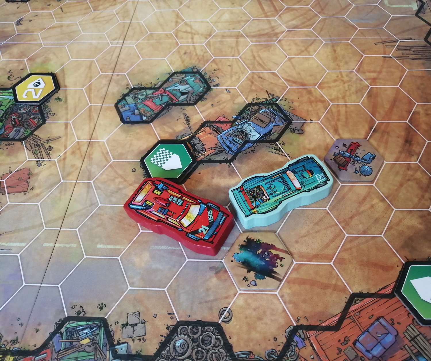 Photo of the board with two cars and some tokens. Tokens fit snugly into the hexes of the board, as do the cars which also fit over two hexes.
