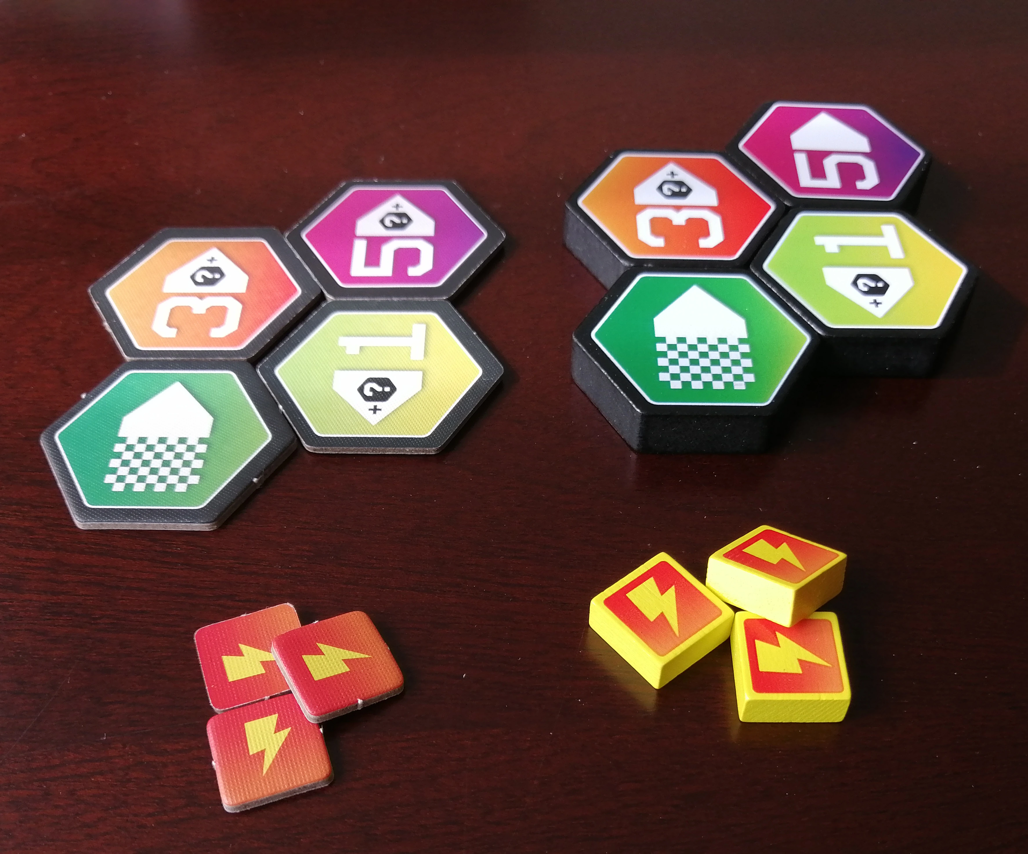 A photo of the gate and damage tokens in the standard versus upgraded version. In standard they are punchboard, and in the upgrade they are wooden and much thicker.