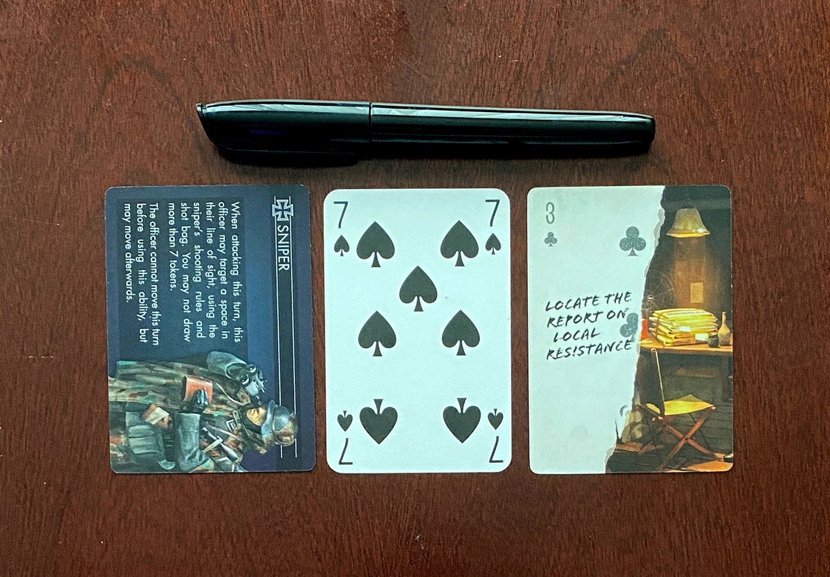 The objective and item cards next to a standard playing card, they are identical in size. The pen is also shown above, and is a similar size to a standard pen.