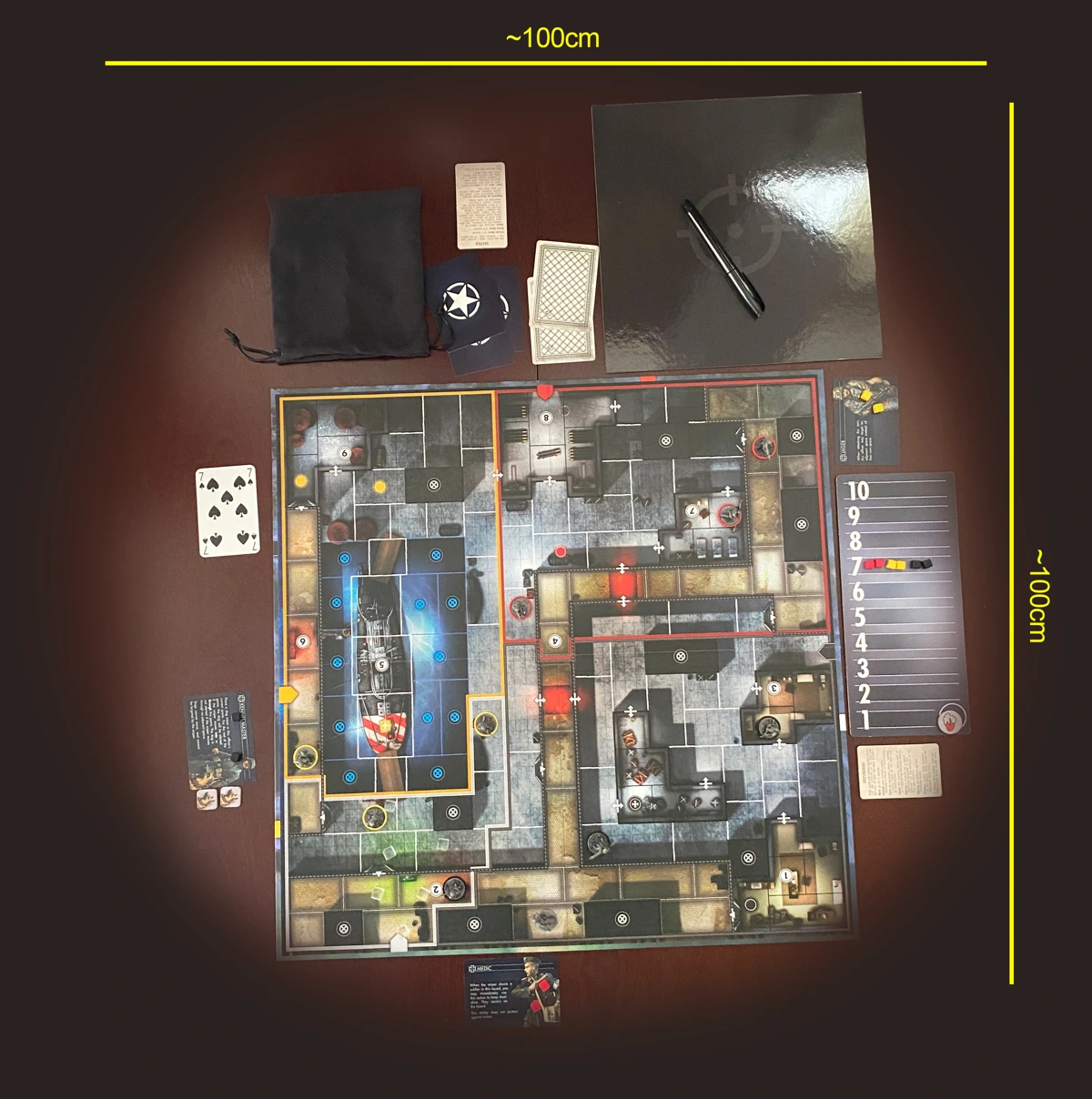 Birds eye view of the game set up on a tabletop, showing all the components laid out together. Measurements overlaid on the image show a width and height of approximately 100cm. 