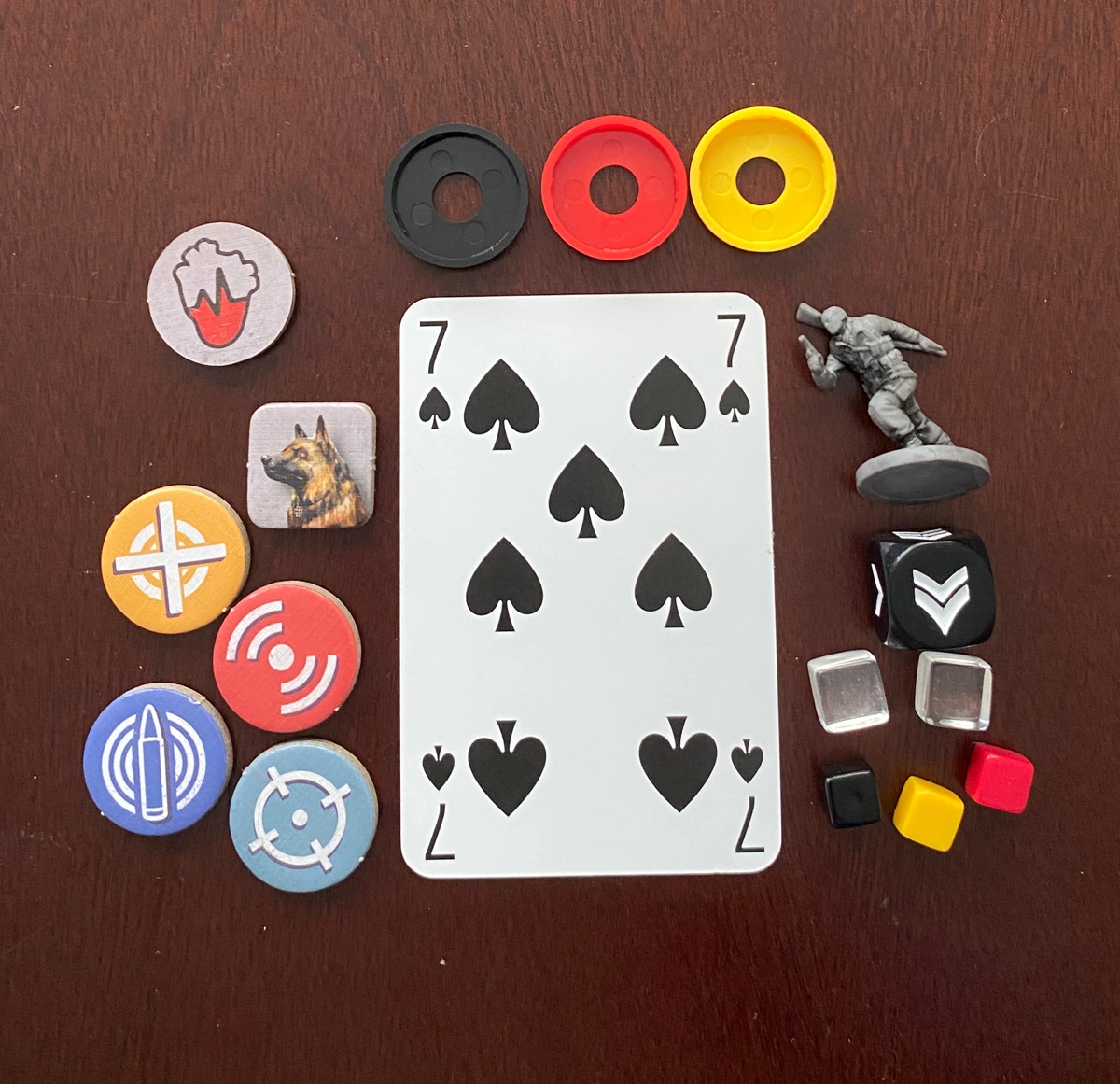 Punchboard tokens, cubes, dice and miniatures lie next to a standard playing card for reference. The tokens are similar in size to the 32mm base of the miniature. The cubes are significantly smaller.